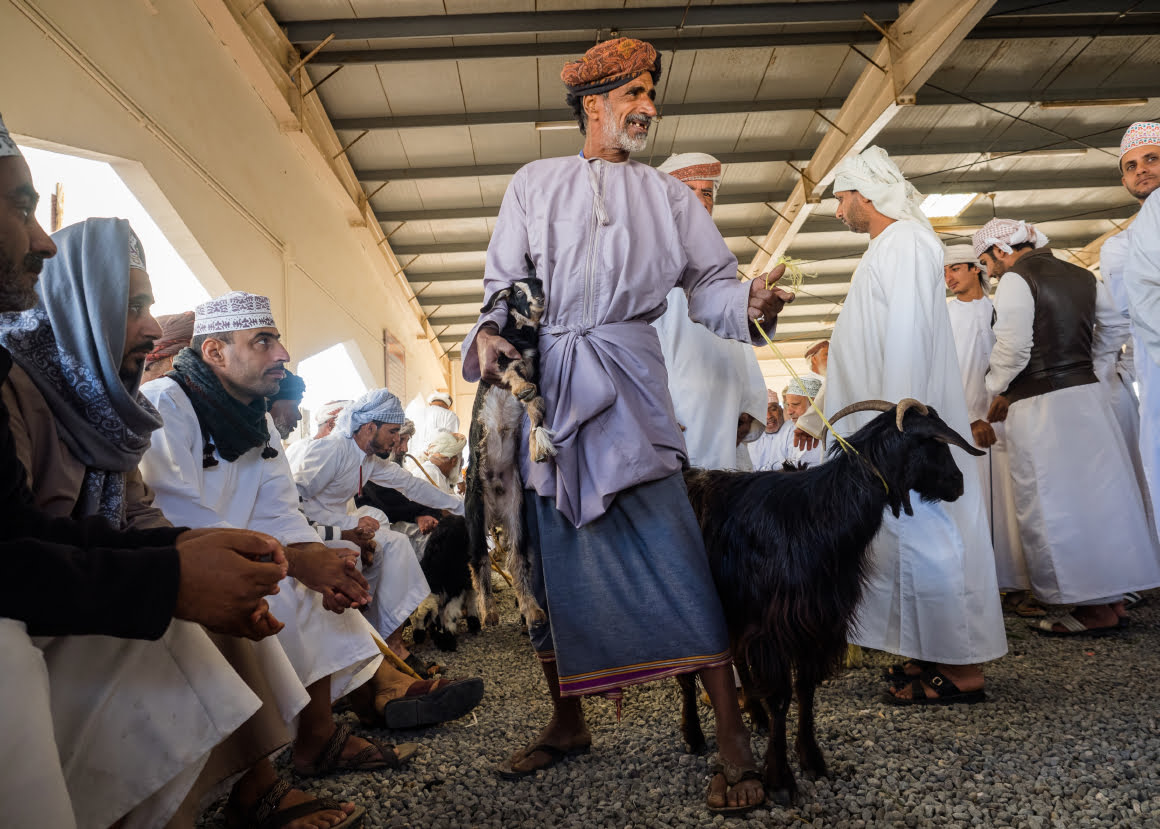 misha szura piwnik-interfoto-omanski-targ-zwierzat-mezczyzna-trzyma kozy-inni-mezczyzni-siedza-i-patrza