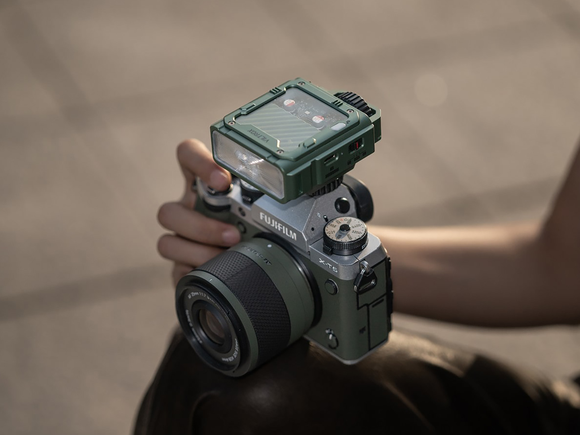 A hand holds a fujifilm camera with viltrox spark z3 flash on top