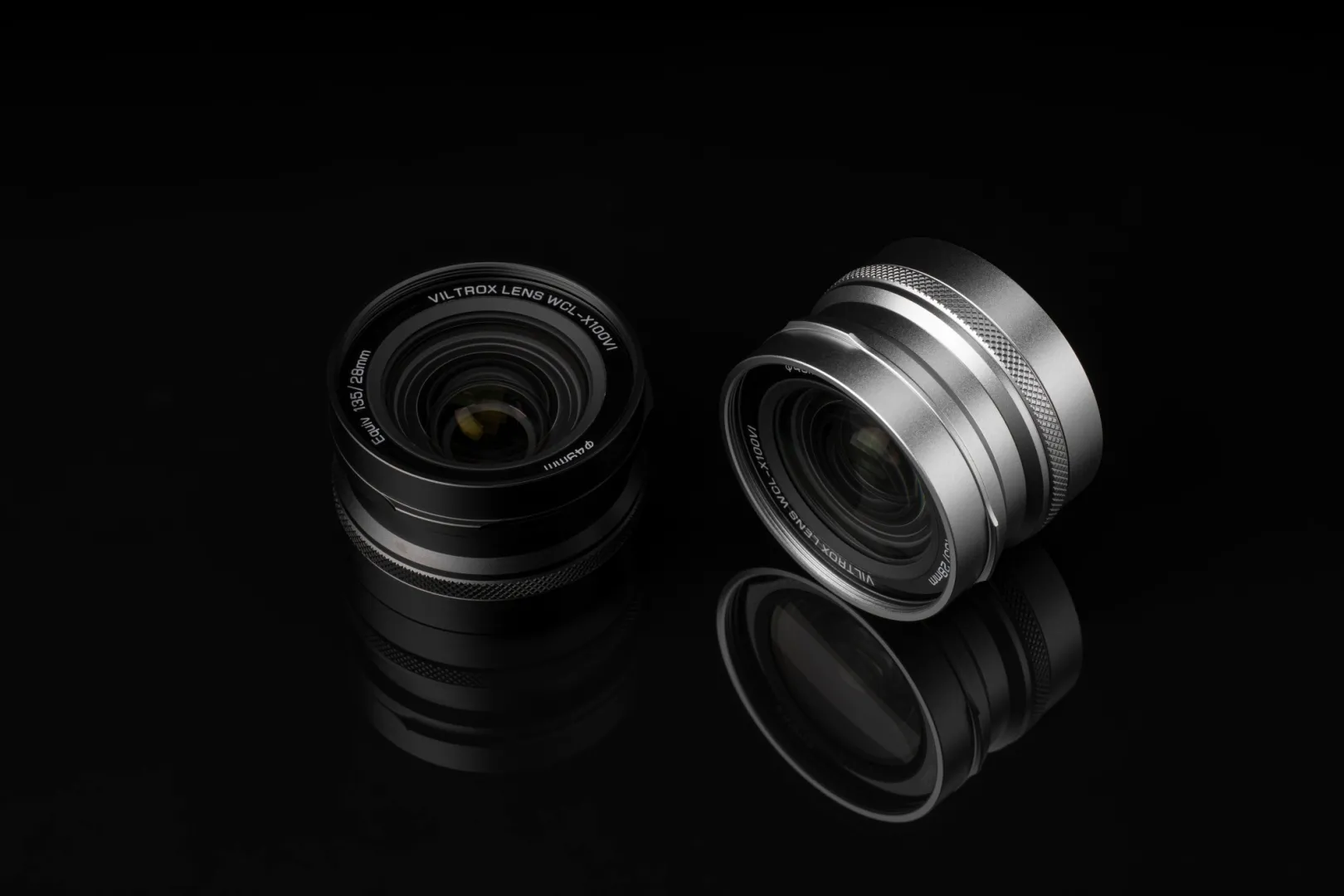 A black and silver viltrox lens are on a reflective black surface with dim lighting